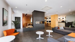 A modern hotel lobby with a reception desk, seating area, and a kitchen in the background. - Hôtel Le Dauphin Montréal - Longueuil (Longueuil)
