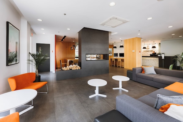 A modern hotel lobby with a reception desk, seating area, and a kitchen in the background.