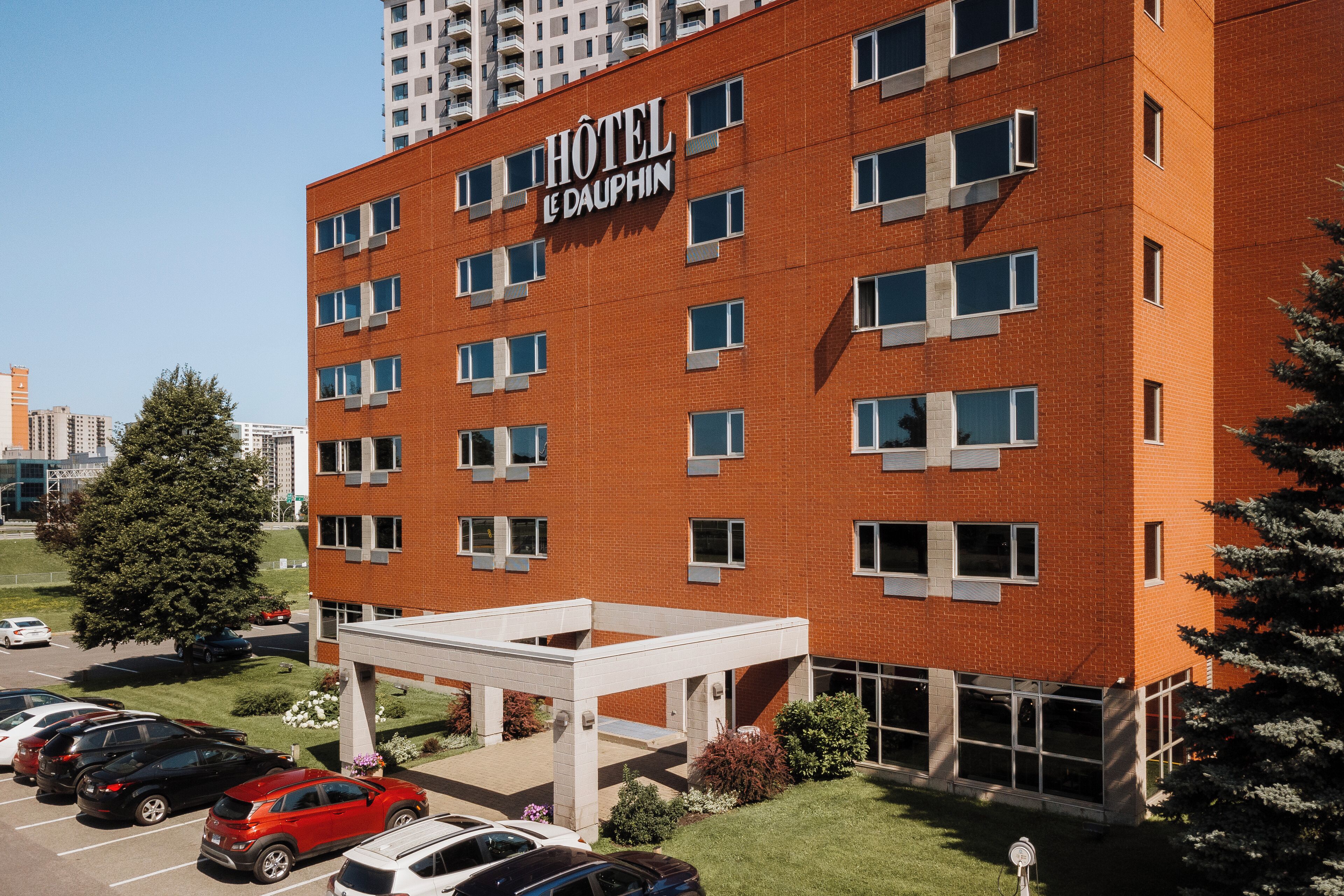 Un hotel con fachada de ladrillo rojo, múltiples ventanas y un estacionamiento con varios coches.