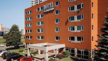 Un hotel con fachada de ladrillo rojo, múltiples ventanas y un estacionamiento con varios coches.