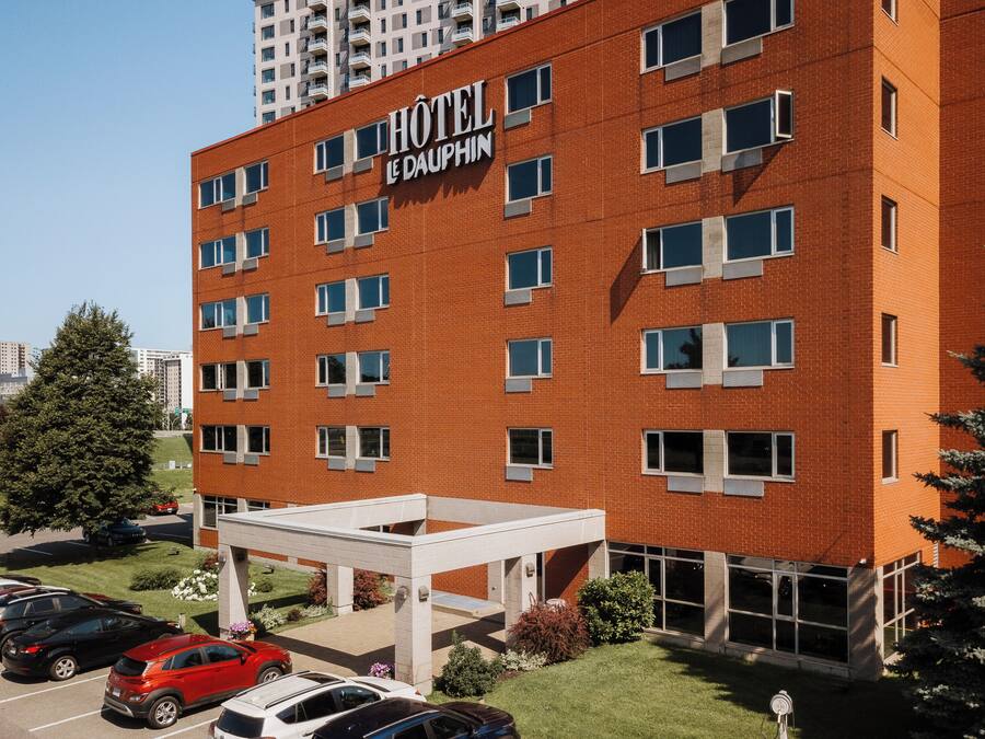 Un hotel con fachada de ladrillo rojo, múltiples ventanas y un estacionamiento con varios coches.