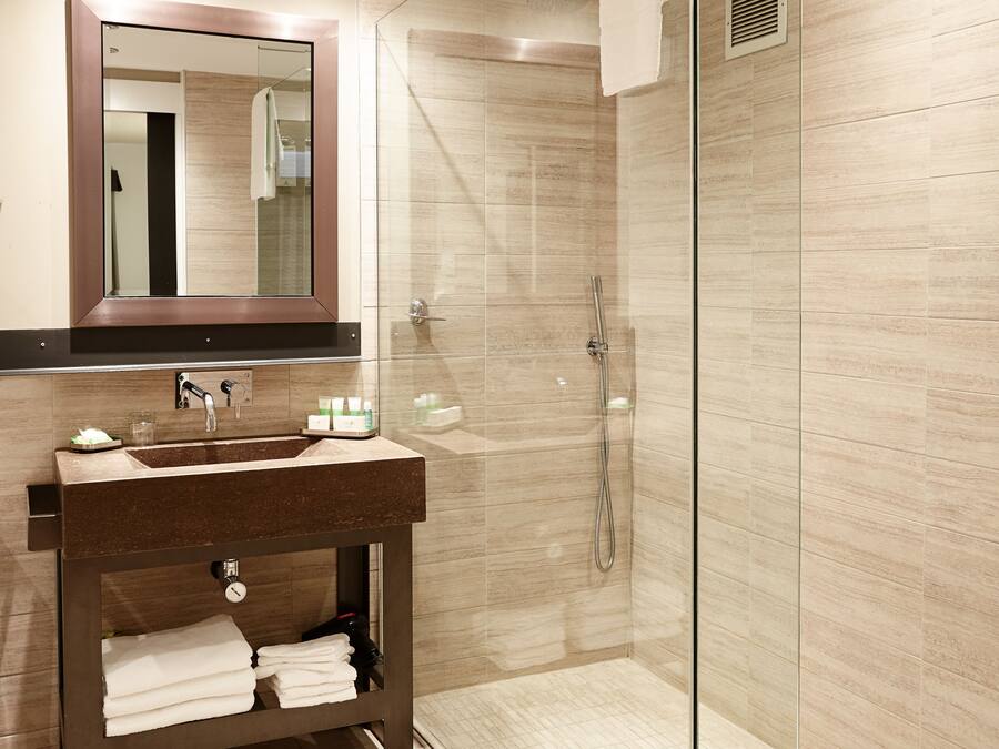 Un baño moderno con ducha de vidrio, tocador de madera con lavamanos y un espejo grande.