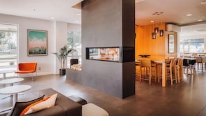 A modern hotel lobby with a central seating area, a dining table, and a large window with a city view. - Hôtel Le Dauphin Montréal - Longueuil (Longueuil)