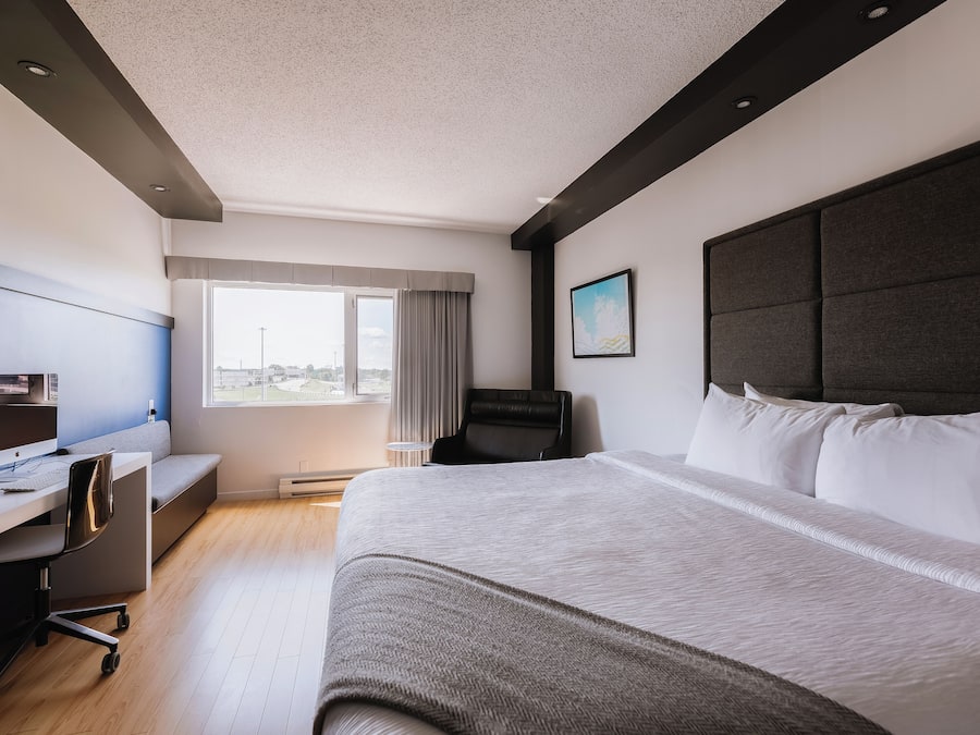 Ein modernes Hotelzimmer mit einem großen Bett, einem Schreibtisch mit Computer, einem Stuhl und einem Fenster mit Blick auf die Stadt.