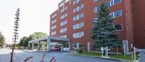 A multi-story red brick building with a covered entrance and a parking area.
