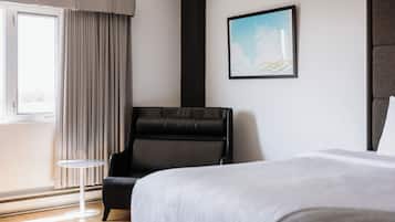 A hotel room with a bed, a black leather chair, a small round table, a window with curtains, and a framed picture on the wall.