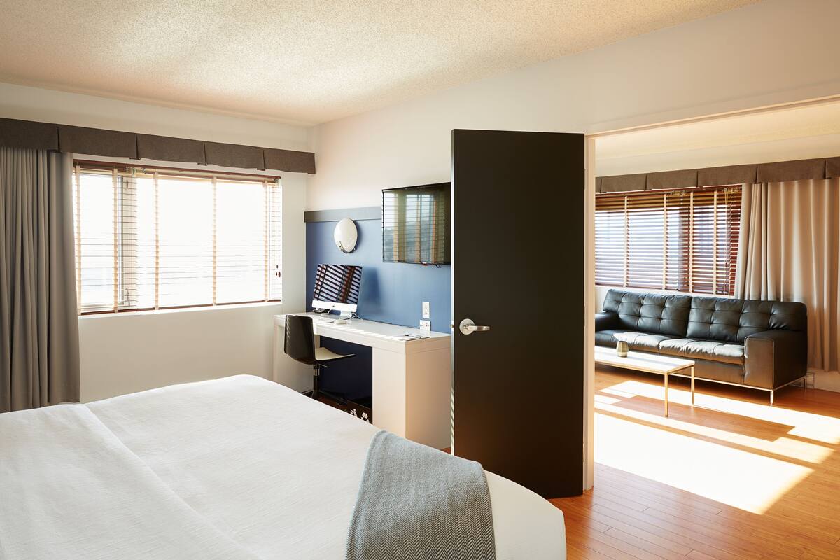 A hotel room with a bed, a desk, a computer, a sofa, and a door.