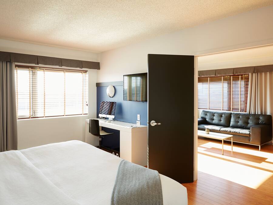 Una habitación de hotel con cama, escritorio, ordenador, sofá y puerta.