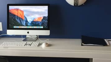 A desk with a monitor, keyboard, and mouse. There is a trash bin with recycling symbols and a black folder on the desk.