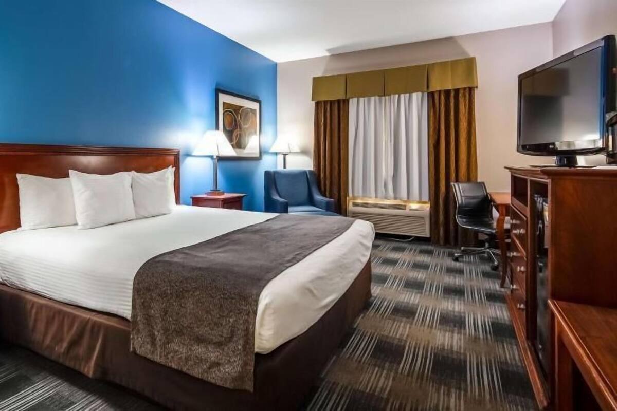 A hotel room with a large bed, two bedside tables with lamps, a TV, a desk, and a chair.