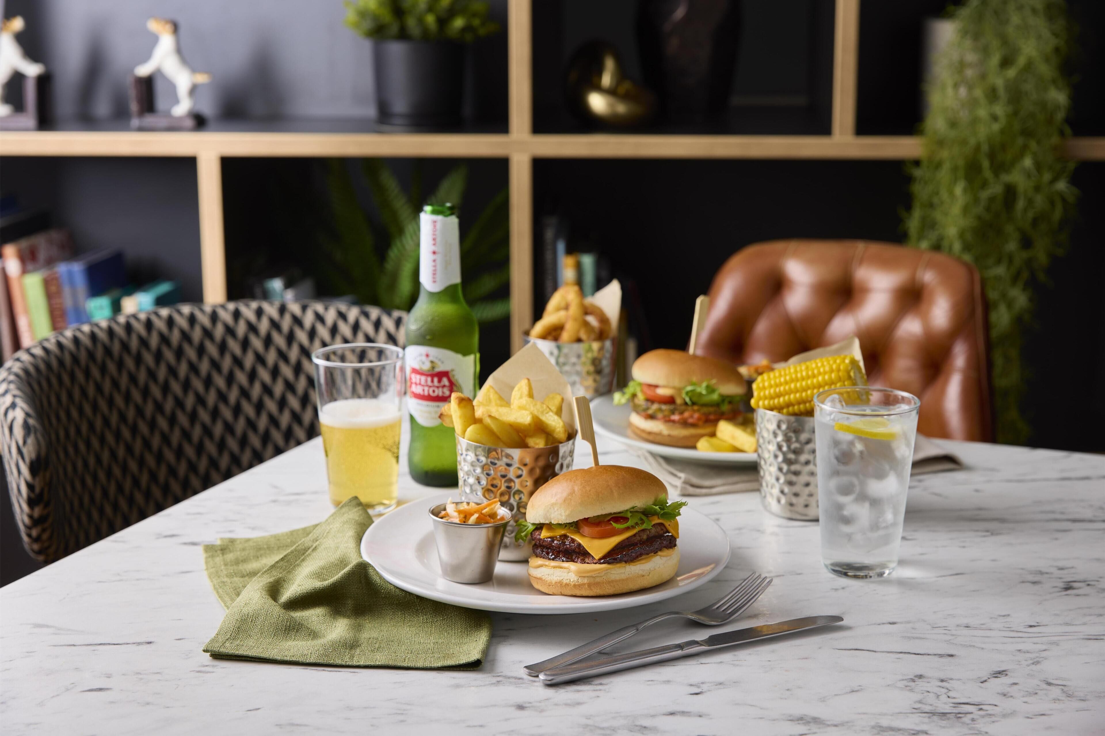 A dining table with a burger, fries, a drink, and a bottle of Stella Artois.