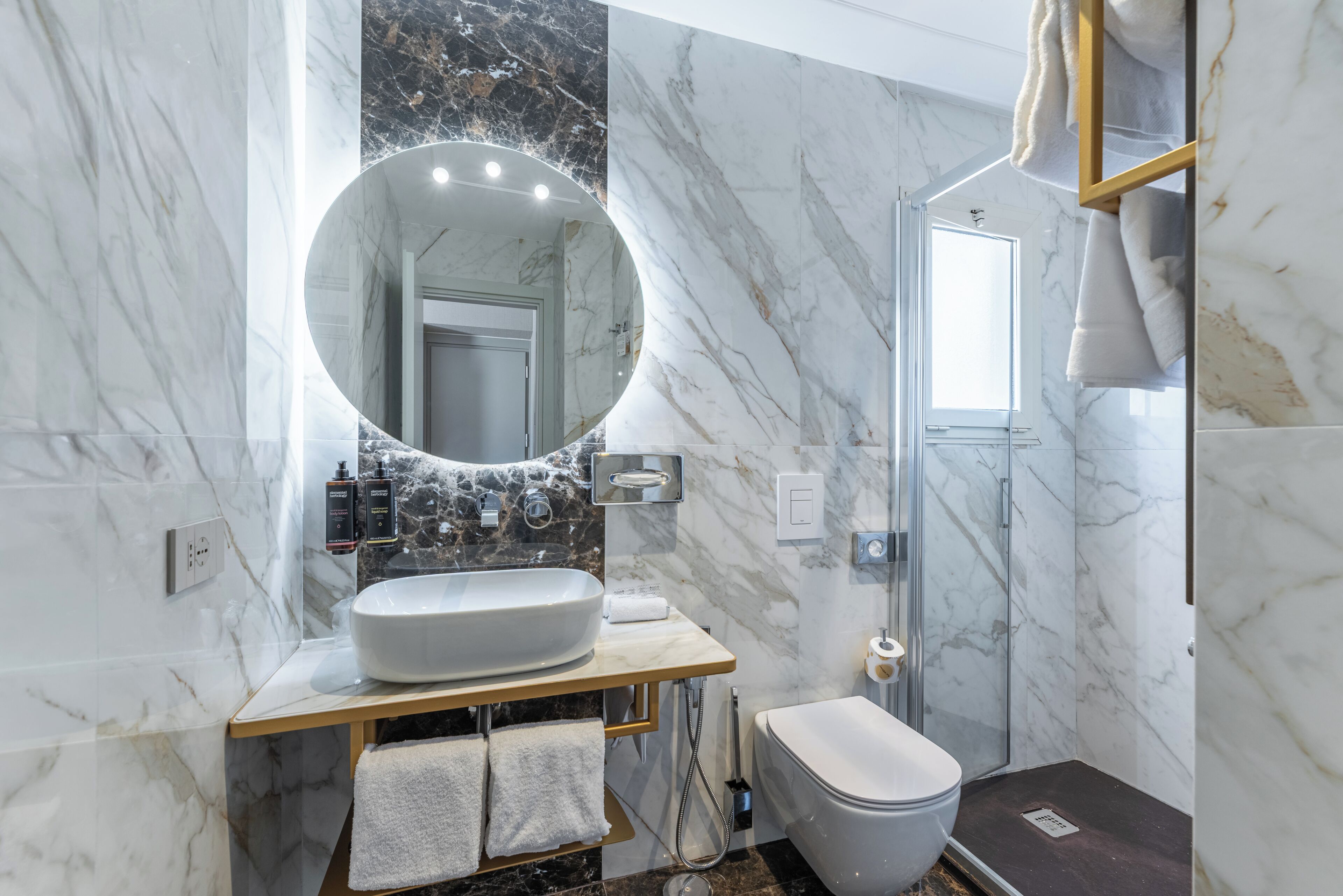 A bathroom with a marble sink, a round mirror, a toilet, and a shower enclosure.
