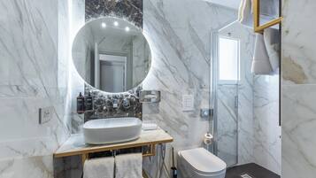 A bathroom with a marble sink, a round mirror, a toilet, and a shower enclosure.
