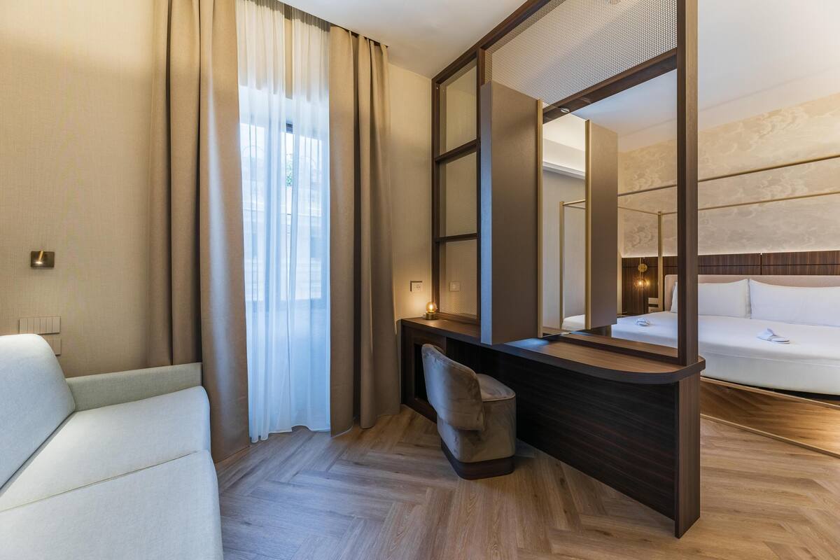 Una camera d'albergo moderna con divano, scrivania, sedia, uno specchio grande e un letto.