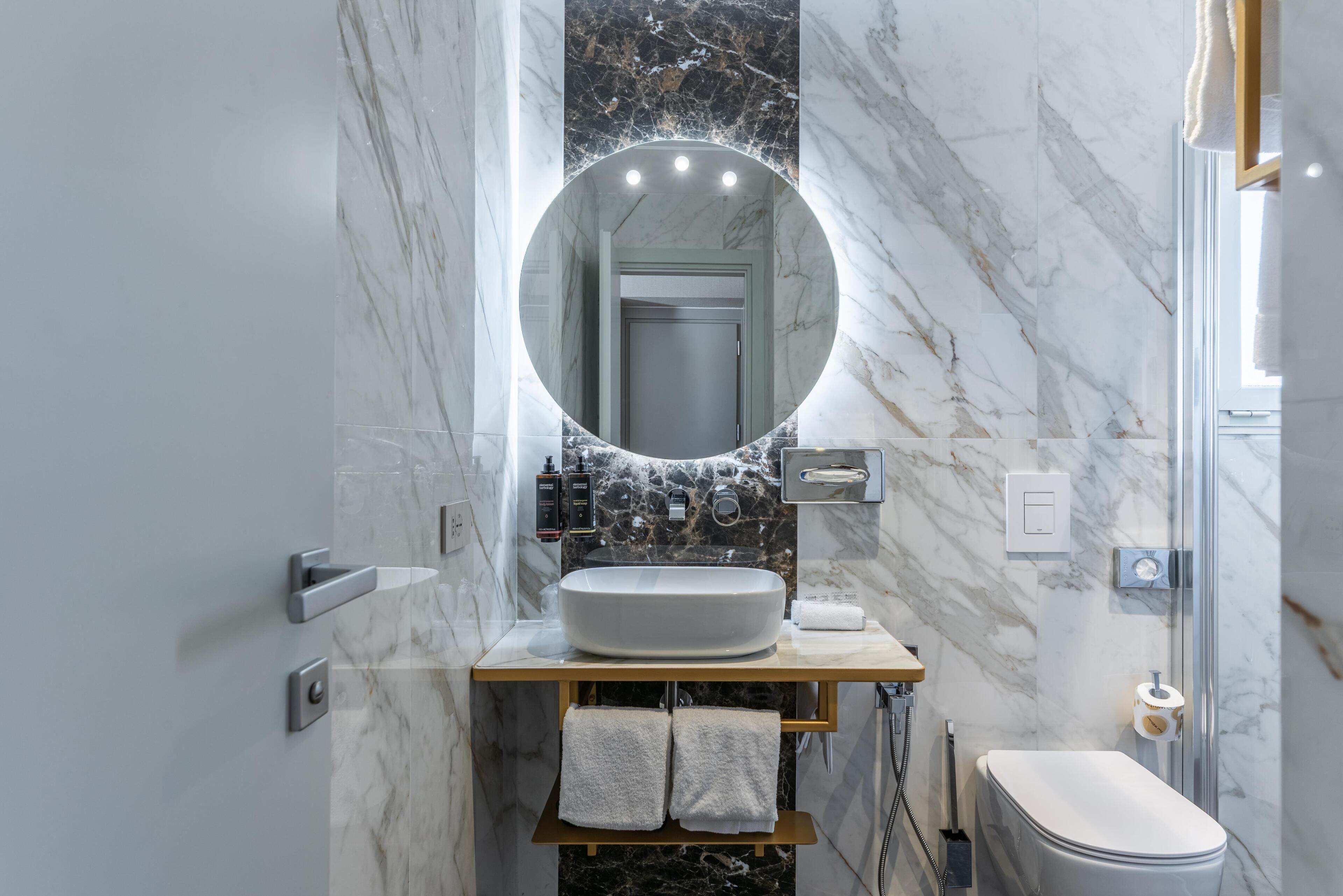 Une salle de bain avec un grand miroir, un lavabo sur colonne, des toilettes et une douche.