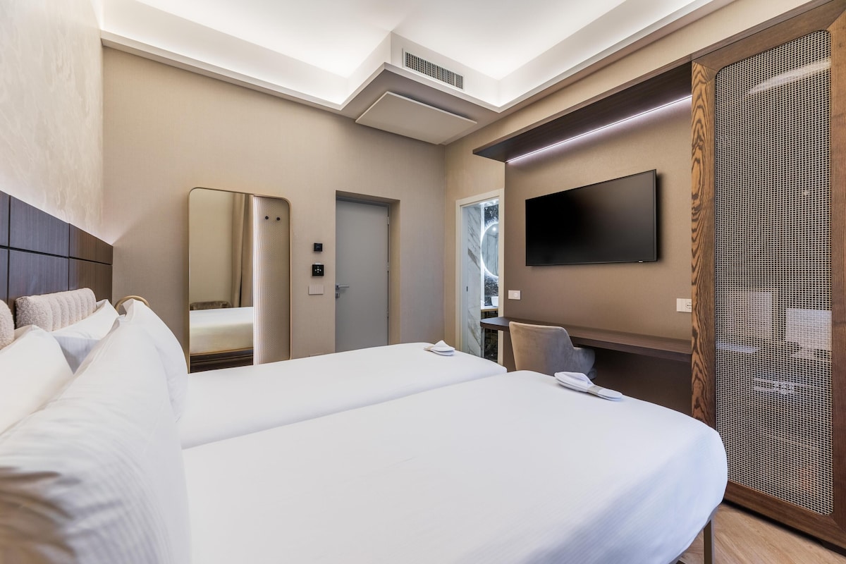 A hotel room with a large bed, a TV mounted on the wall, a mirror, and a wooden partition.