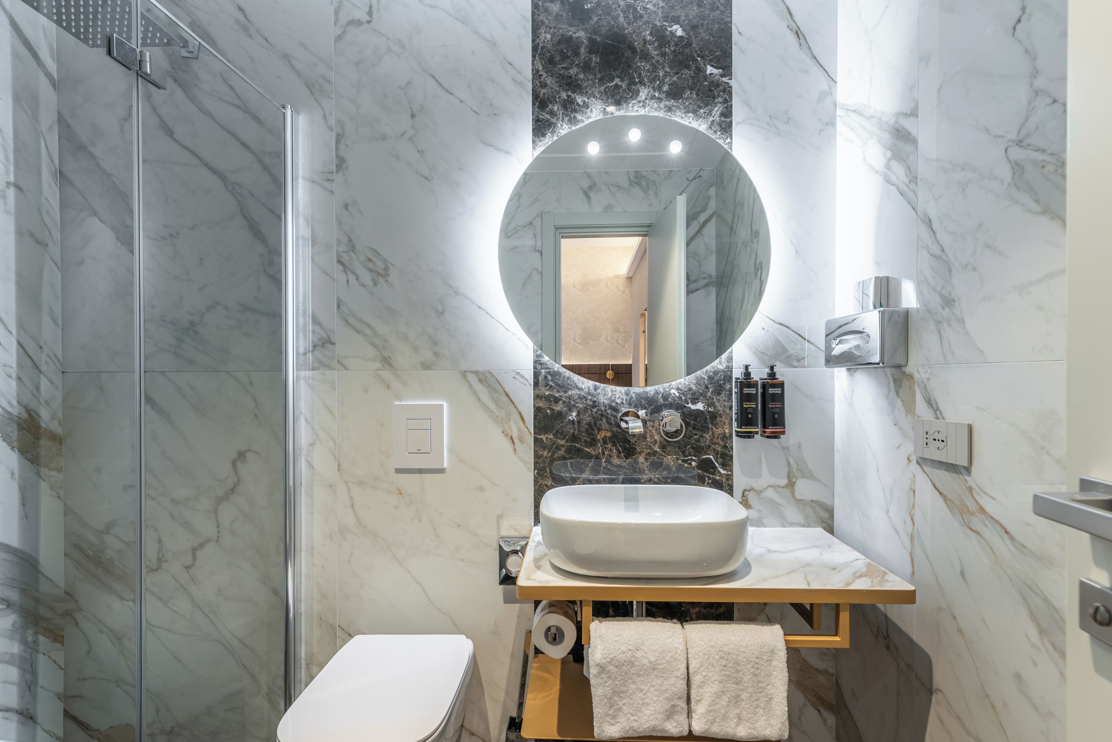 A modern bathroom with a marble vanity, a round mirror, a toilet, and a shower.