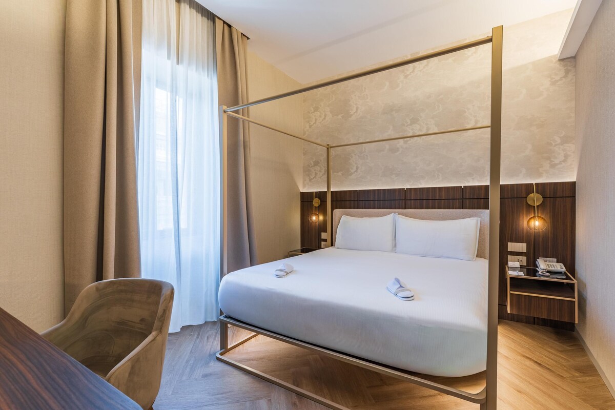 A four-poster bed with a wooden frame, a bedside table with a lamp, and a chair.