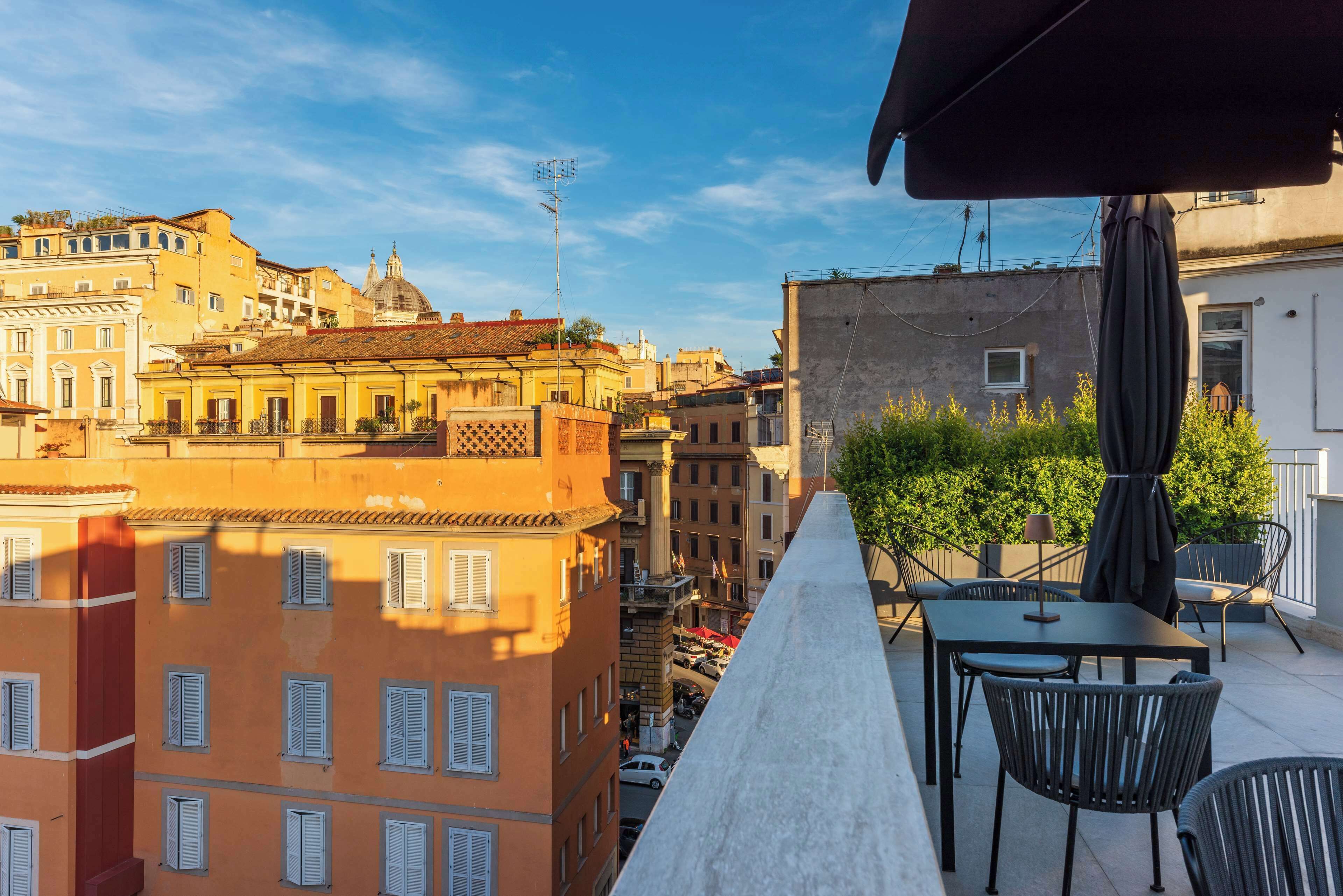 A terrace with outdoor seating, overlooking a cityscape with historic buildings and a clear sky.