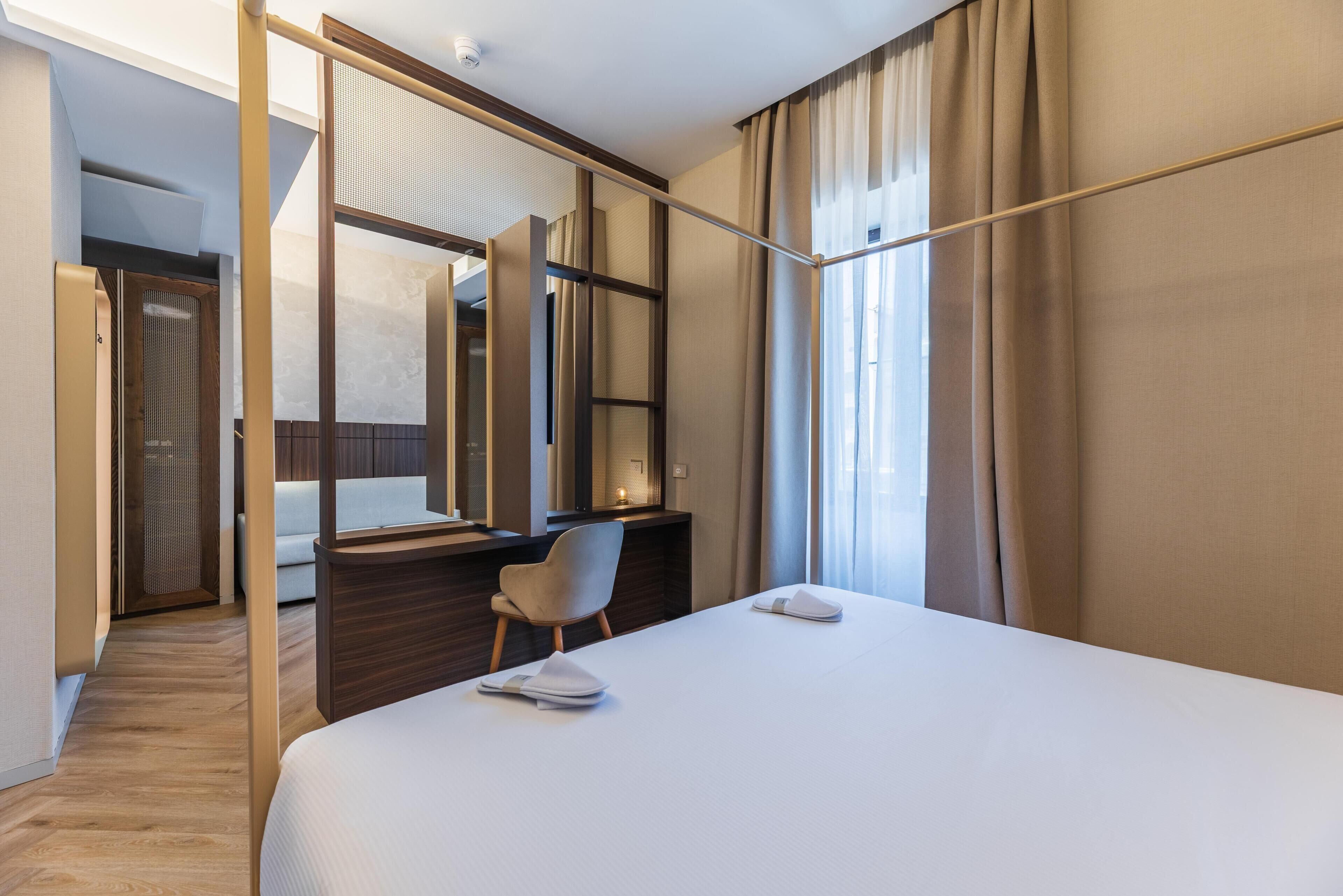 A hotel room with a bed, a desk, a chair, a large mirror, and a view of the outdoors.