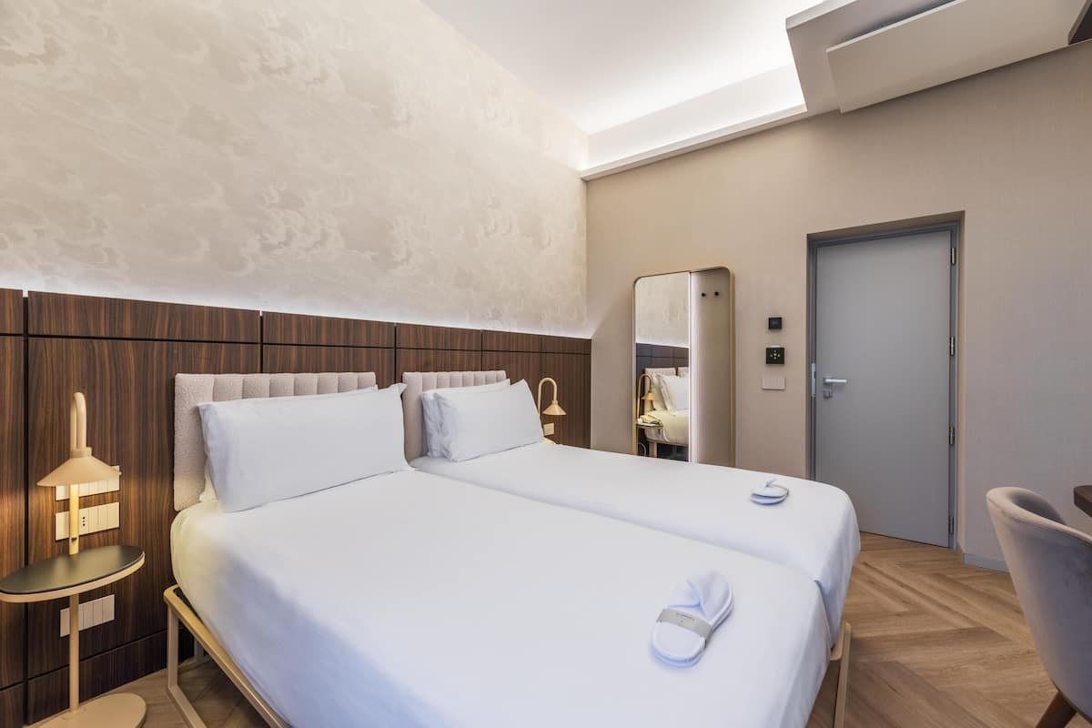 Una camera d'albergo con un letto grande, un comodino, una lampada, una sedia e una porta.