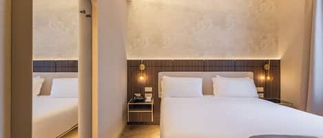 A hotel room with two beds, a wooden headboard, a nightstand with a lamp, and a mirror.