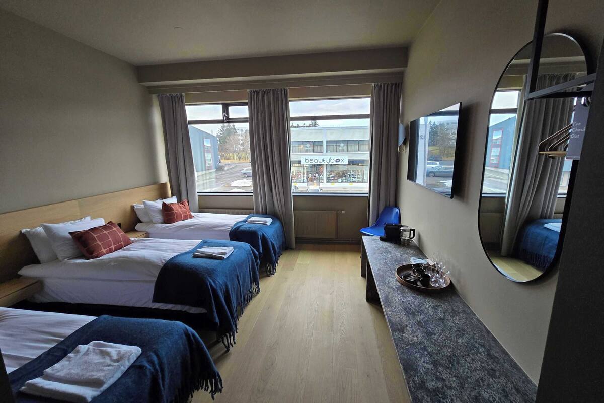 A hotel room with two beds, a desk, a mirror, and a view of the street.