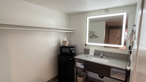 A small, compact bathroom with a white sink, a mirror with a light, a small trash bin, and a black appliance, possibly a microwave. - Hotel Milagro (Chula Vista)
