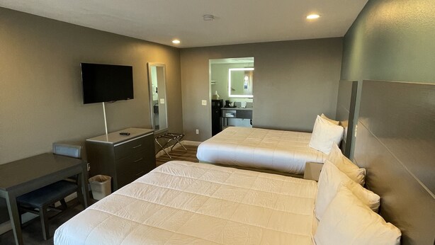 A hotel room with two beds, a desk, a television, and a mirror. - Hotel Milagro (Chula Vista)