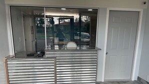 Un área de recepción con puerta de vidrio, mostrador de metal y piso de baldosas.