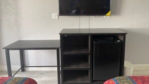 Una habitación con un escritorio negro, un archivador pequeño negro y un televisor montado en la pared.
