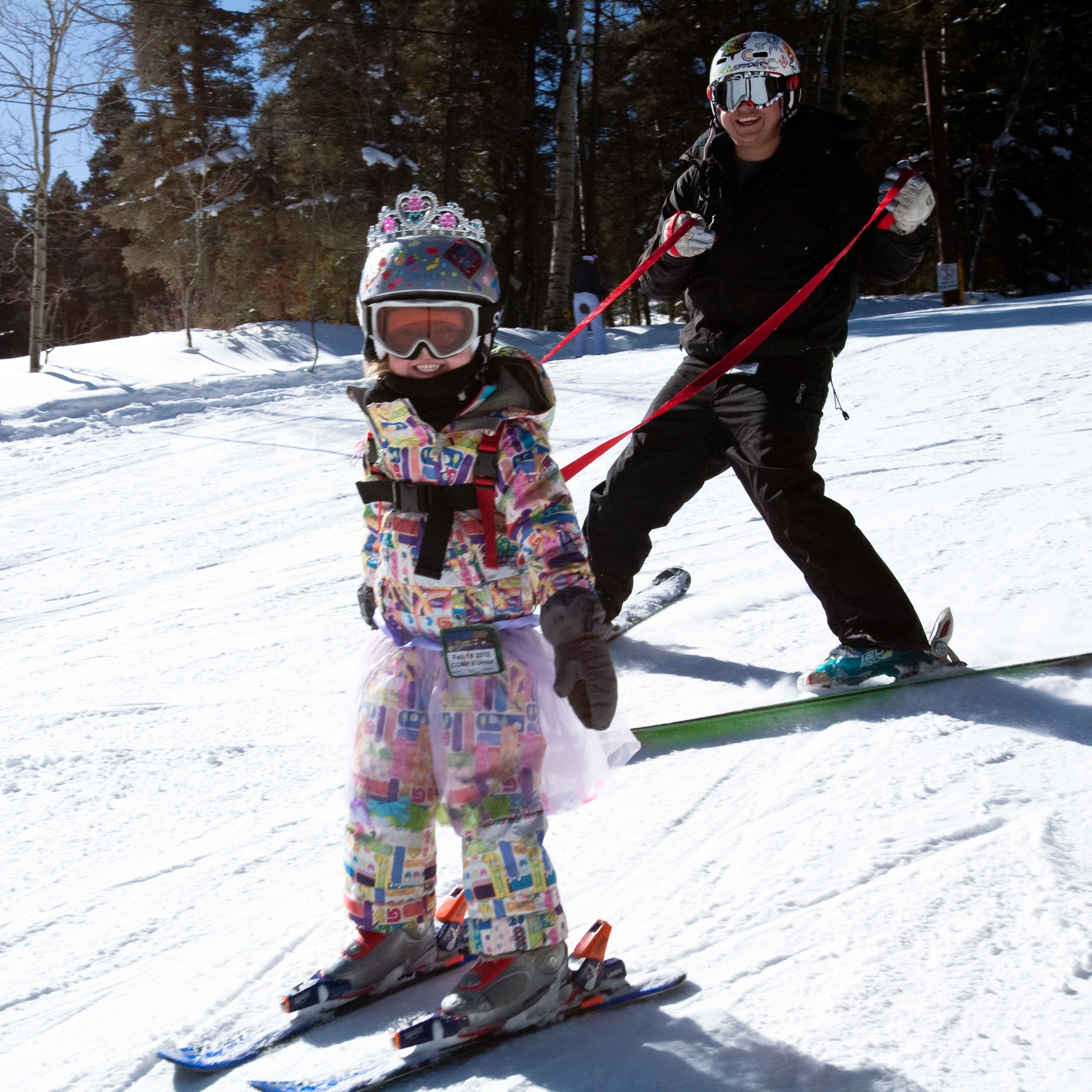 A child and an adult skiing on a snowy slope.