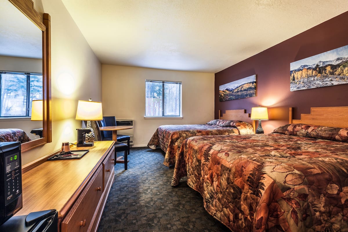 Une chambre d’hôtel avec deux lits, un bureau, une chaise, une commode et un grand miroir.