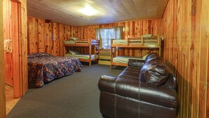 A wooden cabin with bunk beds, a leather couch, and a window with curtains.