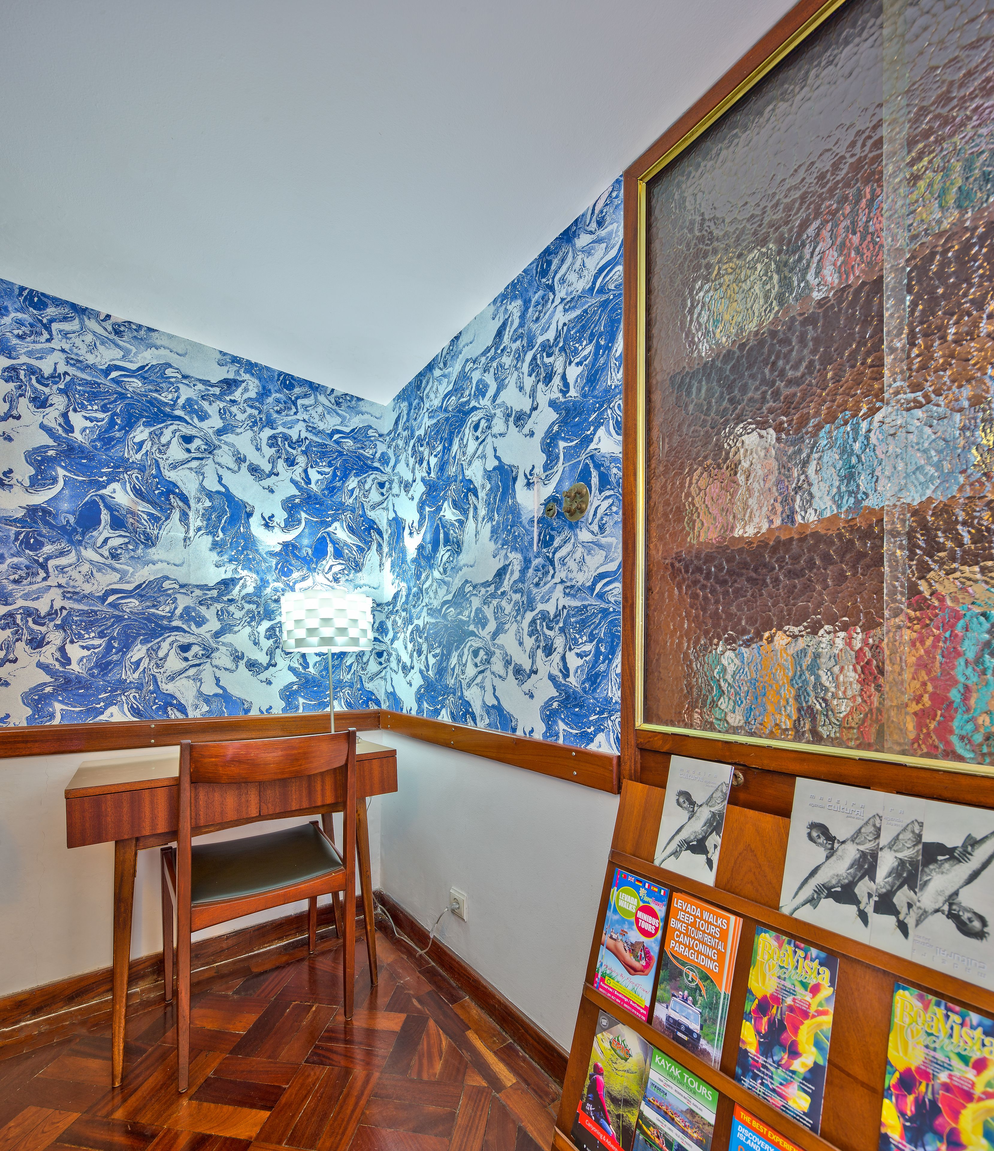 A room with a wooden desk, a chair, a large abstract painting, and a wall with a blue and white marbled pattern.