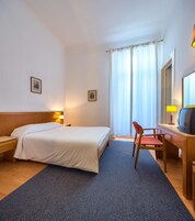 Una camera d'albergo con un letto, una scrivania con una sedia, un televisore e due quadri appesi al muro.