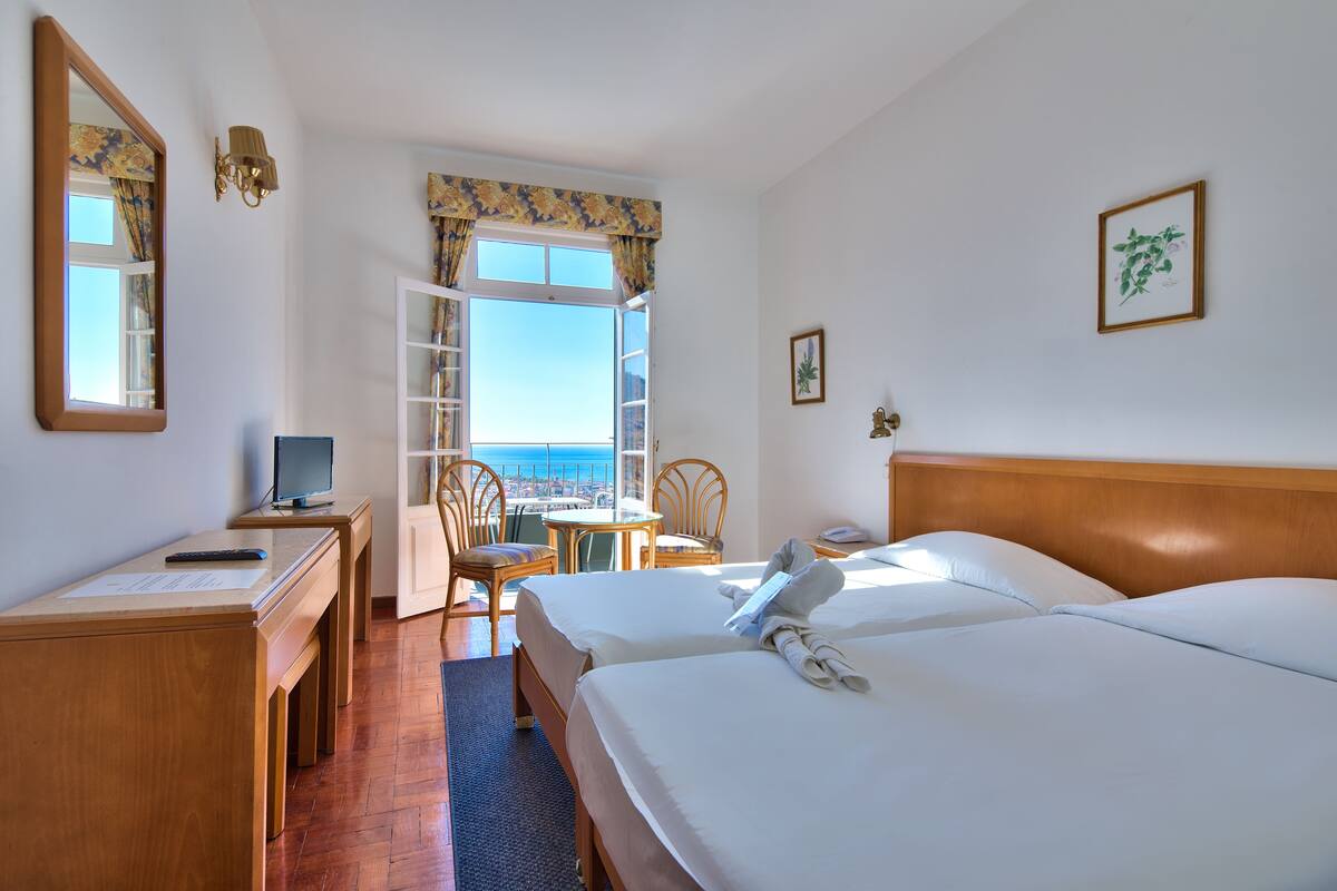 Une chambre d’hôtel avec deux lits, un bureau avec un ordinateur, une chaise et une vue sur la mer.