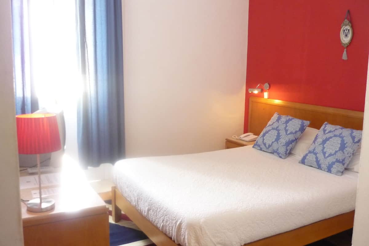 Une chambre d’hôtel avec un lit, une table de chevet, une lampe et une horloge murale.