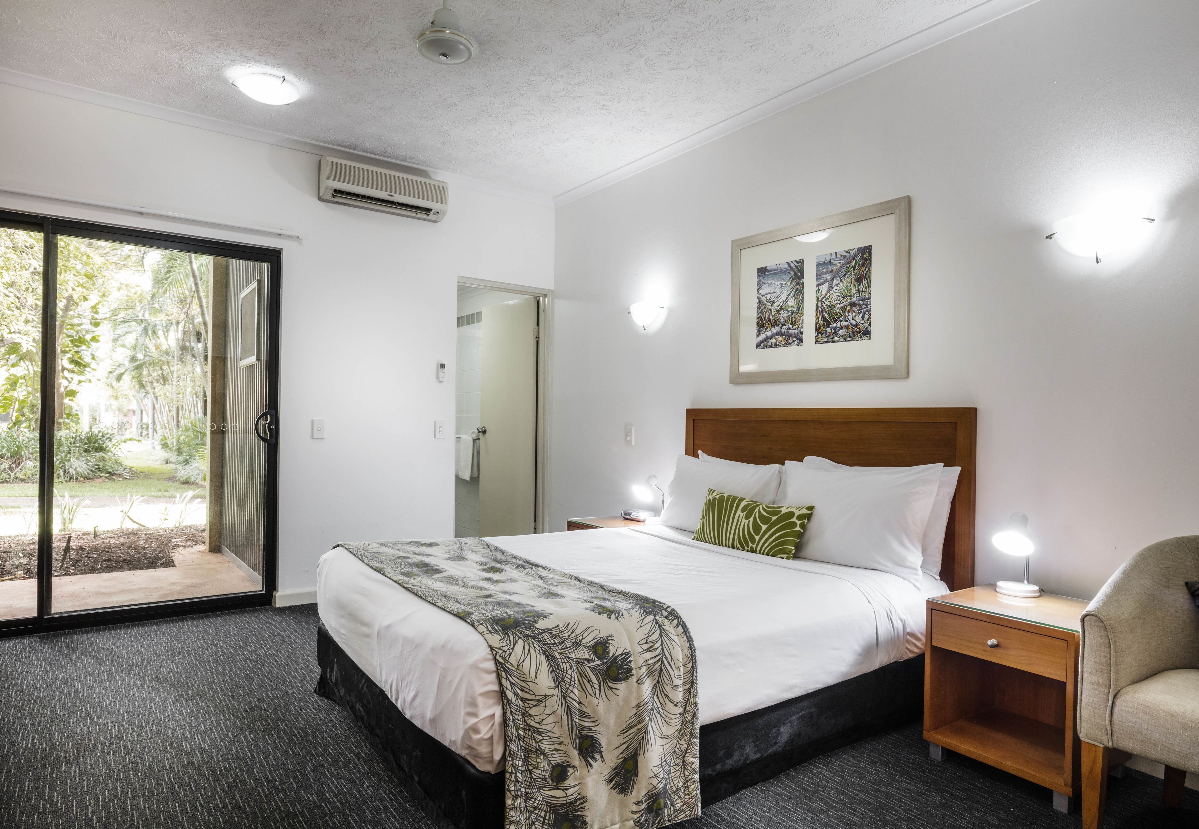 A hotel room with a bed, a nightstand, a chair, a door, and a window.