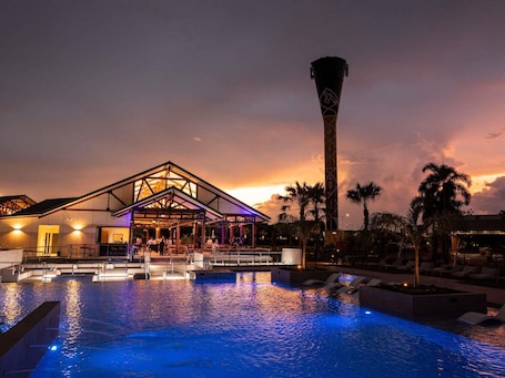 A hotel with a swimming pool, a tall tower, and palm trees.. Mercure Darwin Airport Resort