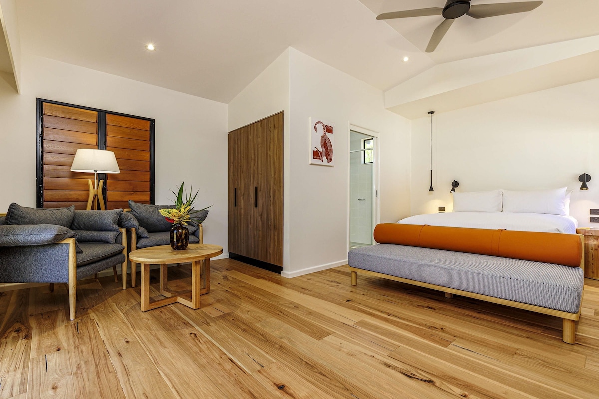Un dormitorio moderno con cama, sofá, una mesita y un ventilador de techo.