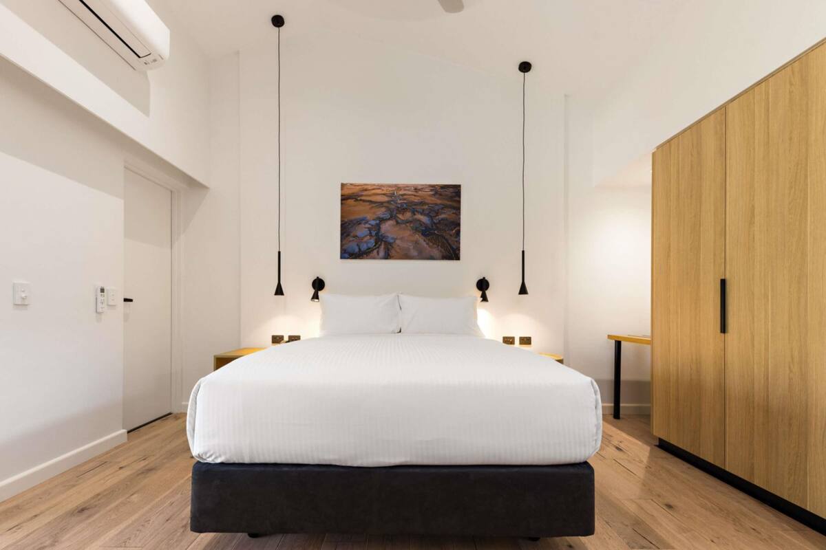 Um quarto moderno com uma cama grande, luminárias pendentes, um quadro na parede e um guarda-roupa de madeira.