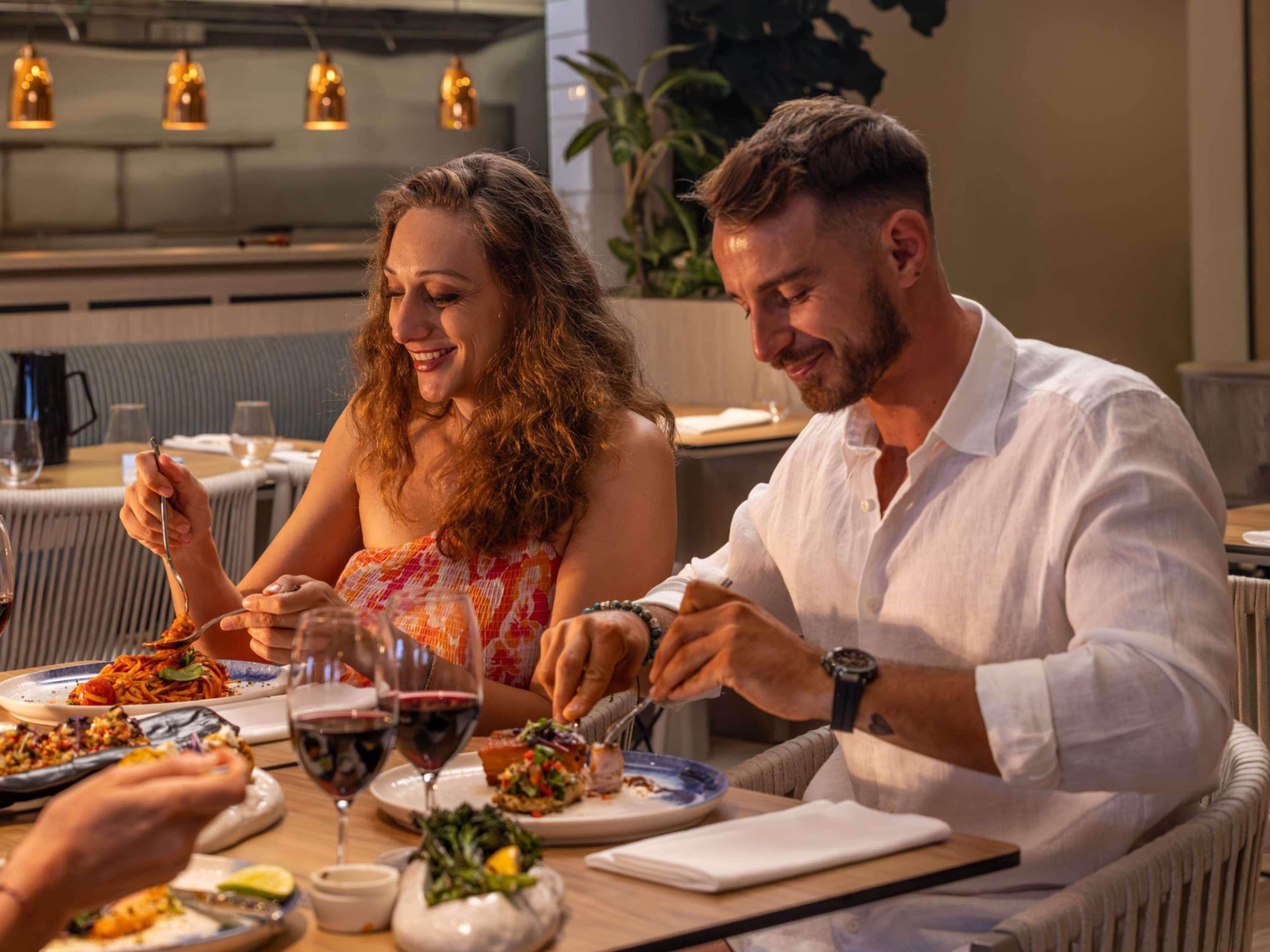 A couple dining at a restaurant with multiple dishes and glasses of wine on the table.