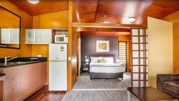 A compact room with a kitchenette, a bed with a headboard, a small table, and a sofa. - Mercure Darwin Airport Resort (Eaton)