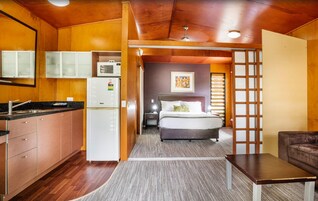 Habitación compacta con kitchenette, una cama con cabecera, una pequeña mesa y un sofá.