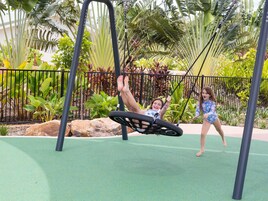 Un parque infantil con columpios y un área cercada con plantas tropicales.