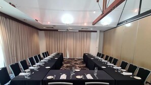 Un salón de conferencias con una larga mesa dispuesta para una reunión, rodeado de sillas.