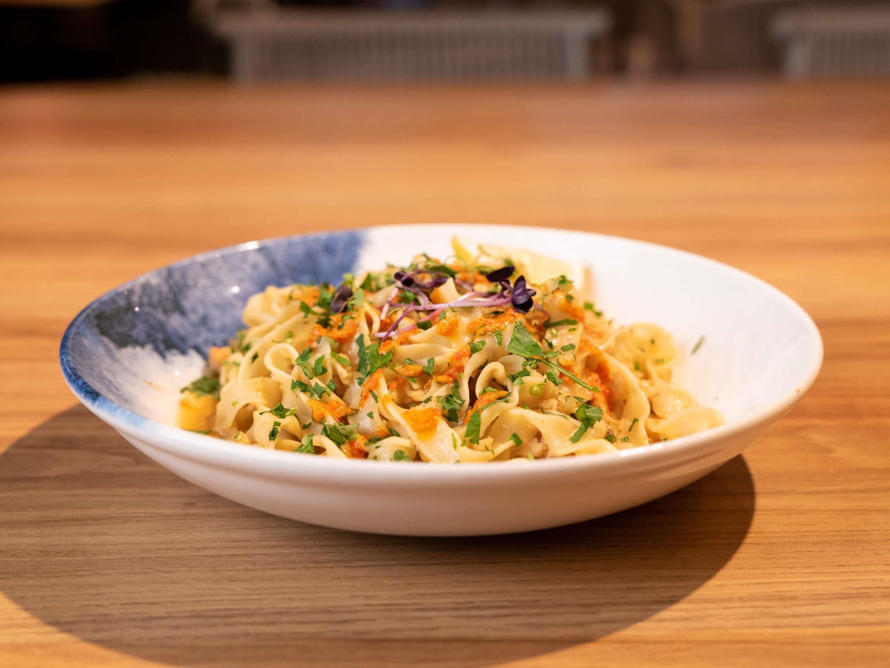 A bowl of pasta with a creamy sauce and garnished with herbs and vegetables.