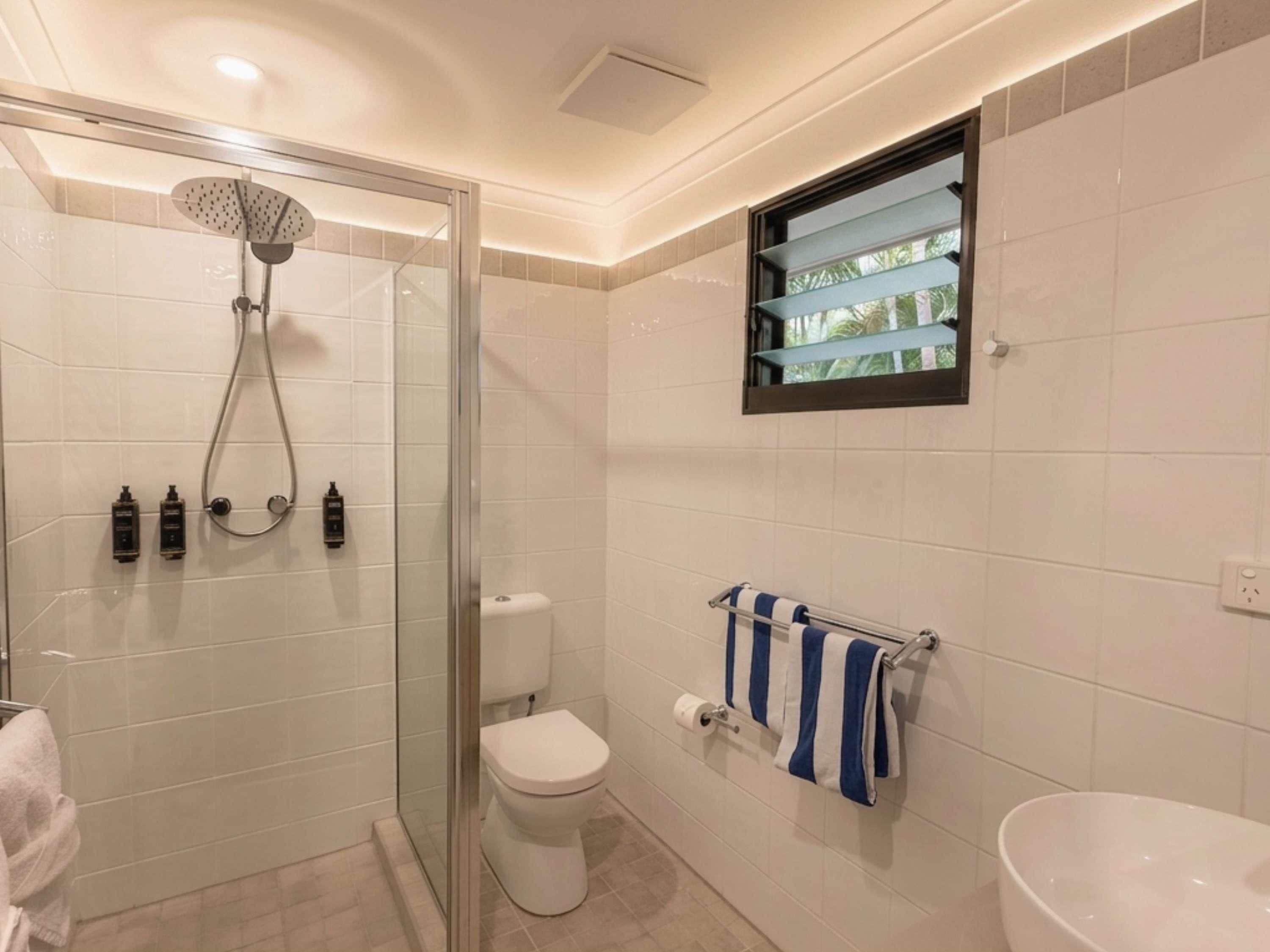 A bathroom with a glass-enclosed shower, a toilet, a sink, and a towel rack with towels.