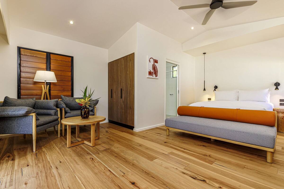 Quarto moderno com cama, sofá, mesinha e ventilador de teto.